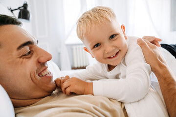 White man playing with his son while lying on bed together