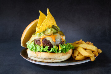 Vertical shot of Guacamole burger with nachos and French fries on a plate.