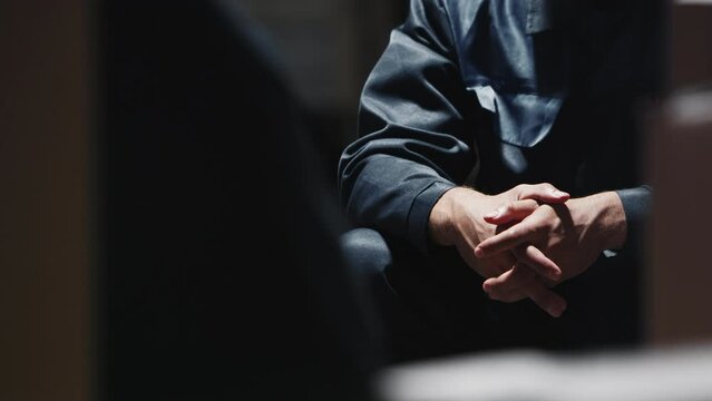 A Man In Prison Clothes Sits On Boxes And Nervously Picks His Fingers.