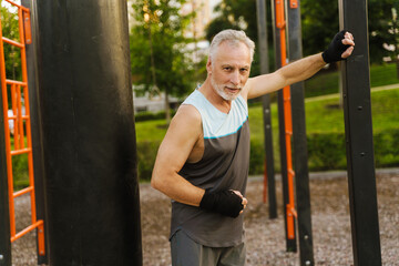 Gray mature man working out with punching bag on playground