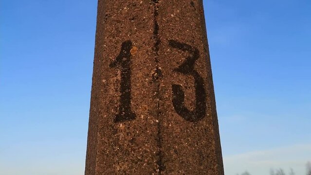 The number 13 is drawn in black paint on a pole close-up against the blue sky. Symbol of Friday the 13th. Sign. Distance marker. House number. Baker's dozen. Folk omen. Nobody. Fatalism. Numerology.