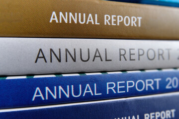 A stack of annual reports from public listed companies received by shareholders to review and evaluate the company business and financial performance of the previous year. Macro closeup view.