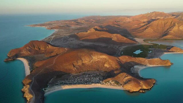 Cinematic wide revealing drone shot of Balandra Beach, view of red hills, turquoise waters, white-sand beaches, and mountains during sunset