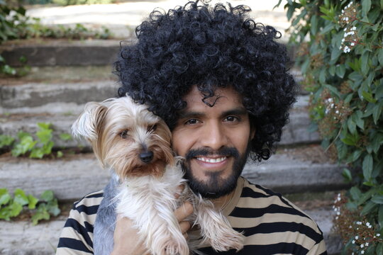 Beautiful Hispanic man with curly hairstyle holding Yorkshire terrier dog - Powered by Adobe