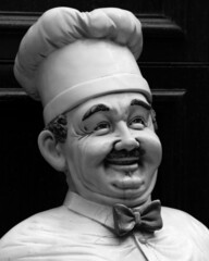 Closeup shot of a male cook statue dressed in uniform with a mustache and a big smile in greyscale