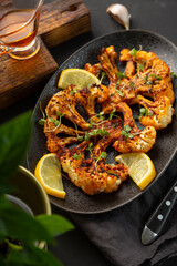 Vegetarian cauliflower steaks with microgreens and lemon on the black background, close up vertical photo. Alternative to traditional meat steaks for vegans.