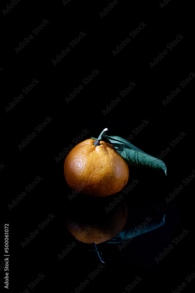 Sticker Vertical closeup of a tangerine with a leaf isolated on a black background with a reflection