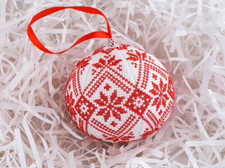 Cross stitched christmas ornament on white shredded wrapping paper background.