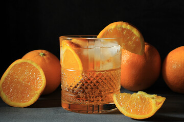 Closeup shot of a spritz cocktail in a glass with oranges on a grey surface on a black background