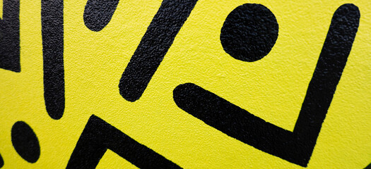 Fragment of the yellow painted wall with geometric black colors graffiti painting in the street....