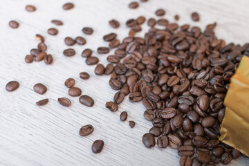 Coffee beans from the package are scattered on the table with texture. diagonally