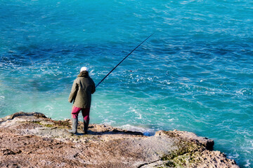 Fototapeta na wymiar Fisherman stood on a rocky beach fishing with a rod in winter