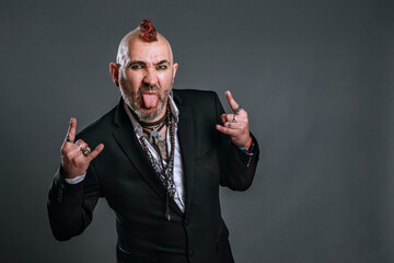 punky-style man dressed in suit jacket sticks out his tongue and makes horn signal with his hands...