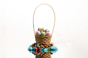 Easter Egg Basket filled to the Brim With eggs and chocolates for the Easter holiday, hand woven bamboo basket with stunning textures on a reflective surface with a perfect mirror image.