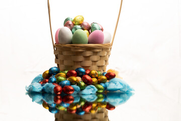 Fototapeta na wymiar Easter Egg Basket filled to the Brim With eggs and chocolates for the Easter holiday, hand woven bamboo basket with stunning textures on a reflective surface with a perfect mirror image.
