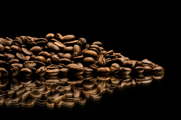Raw un grounded coffee beans laying on a heap on a reflective surface on a black background 