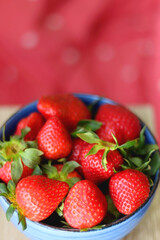 Bowl of fresh strawberries. Red bedding in the background. Selective focus.