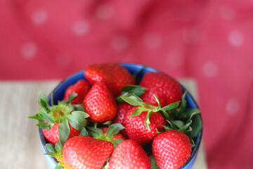 Bowl of fresh strawberries. Red bedding in the background. Selective focus.