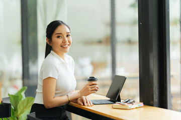 Beautiful young asian business woman drinking coffee and using laptop computer while working in office.