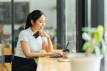 smiling woman paying online, using laptop, holding plastic credit card, sitting on coffee shop, Asian female shopping, making secure internet payment, browsing banking service.