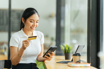 smiling woman paying online, using laptop, holding plastic credit card, sitting on coffee shop, Asian female shopping, making secure internet payment, browsing banking service.