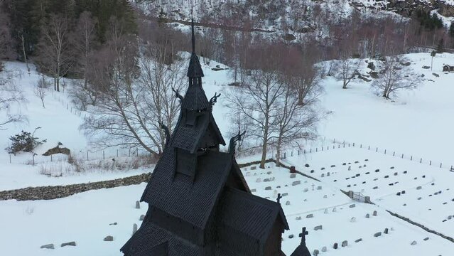 Borgund stave church winter aerial - Slowly descending from top of tower to reveal whole church and entrance - Surrounded by snow covered graveyard