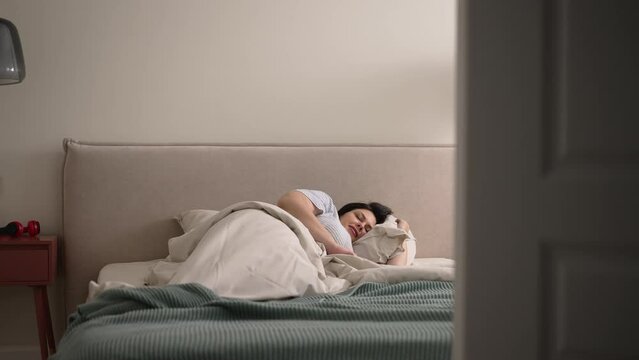 Young overweight woman is waking up and smiling while lying on bed in apartment bedroom spbd. 4k Beautiful American female sleeps and wakes up with happy smile, stretches her body and lies on blanket