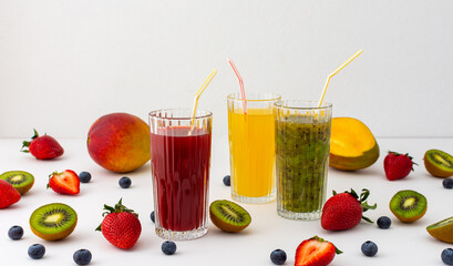 Strawberry, mango, blueberry juice and kiwi juice in glasses with a straw, fruit scattered on the...