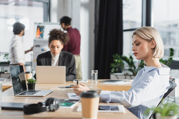 Young businesswoman looking at documents near coffee to go and laptop in office.