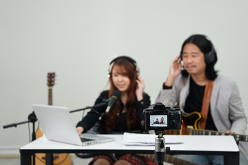 video camera recording man and woman musician live streaming music online by social media in studio,selective focus at camera