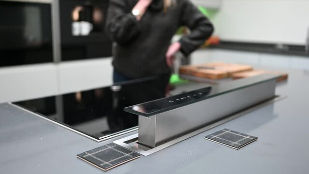 Pop up extractor fan rising in kitchen island set against out of focus background of kitchen with coffee maker in use.