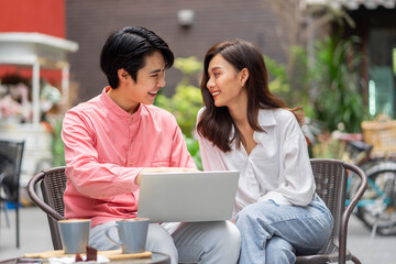 Young Asian couple with laptop computer at coffee shop. coworkers, or business partners have fun using smartphone together, cafe lifestyle.