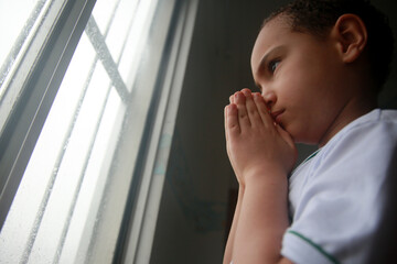 salvador, bahia, brazil - april 20, 2022: white ethnicity child praying next to an apartment window...