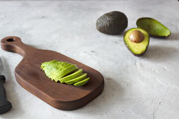Cut avocado on the brown wooden board with avocados on the background