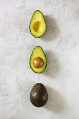 Cut and whole avocado laying on a vertical line on the gray table. Top view.