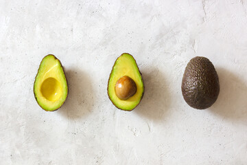 Cut and whole avocado laying on a line on the gray table. Top view.