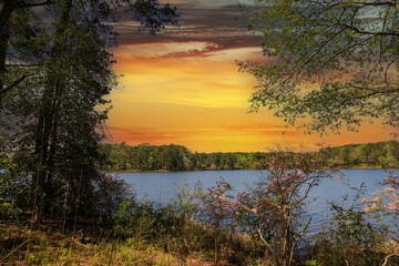 Naklejka na ściany i meble a gorgeous blue simmering lake surrounded by lush green trees and plants with a stunning sunset and powerful clouds at Callaway Gardens in Pine Mountain Georgia USA