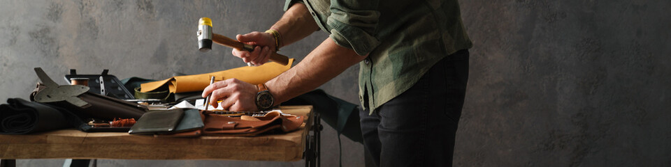 Bearded focused craftsman working with leather while standing at table