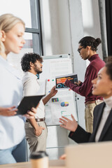 Obraz premium Side view of interracial business people working near flip chart in office.