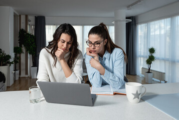 Two young business females freelancer colleagues discuss job chat hold pleasant conversation at home office workplace. Young woman project manager assist coworker explain work in corporate app