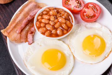 English breakfast with fried eggs, bacon, beans, tomatoes, spices and herbs