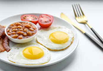 English breakfast with fried eggs, bacon, beans, tomatoes, spices and herbs