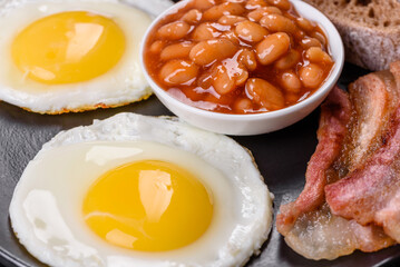 English breakfast with fried eggs, bacon, beans, tomatoes, spices and herbs