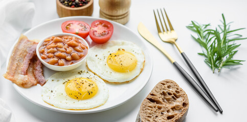 English breakfast with fried eggs, bacon, beans, tomatoes, spices and herbs