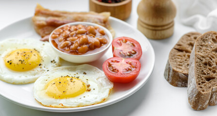 English breakfast with fried eggs, bacon, beans, tomatoes, spices and herbs