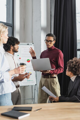 African american businessman holding laptop near interracial colleagues during meeting in office.