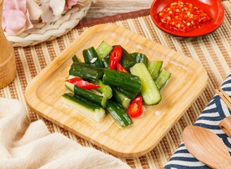 cold cucumber with red chili in a wooden dish with spoon and chopsticks isolated on mat side view on wooden table taiwan food