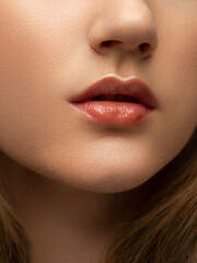 Close-up of woman's lips with fashion natural beige lipstick makeup. Macro sexy pale lipgloss make-up . Gentle pure skin and wavy blonde hair. Cosmetology, Spa, increase in lips