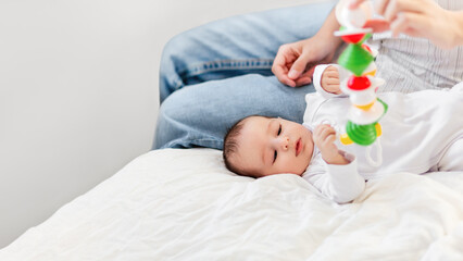 Mother plays with little son or daughter. Woman holds baby first toy - colorful rattle toy. Little...