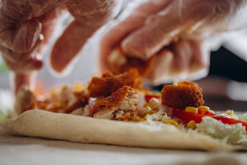 Men's hands wrapping traditional shawarma wrap with chicken and vegetables